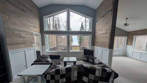 A cozy living room with a large window, a TV, a sofa, and a coffee table. - Cottage On The Lake (Pine Dock)