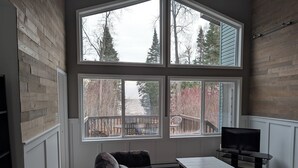 A cozy living room with a large window, a flat-screen TV, and a dark floral sofa. - Cottage On The Lake (Pine Dock)