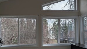 A bedroom with a bed, a desk, and three windows offering views of a forested area. - Cottage On The Lake (Pine Dock)