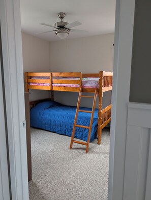 A small, single-bedded room with a wooden bunk bed, a ceiling fan, and a ladder.
