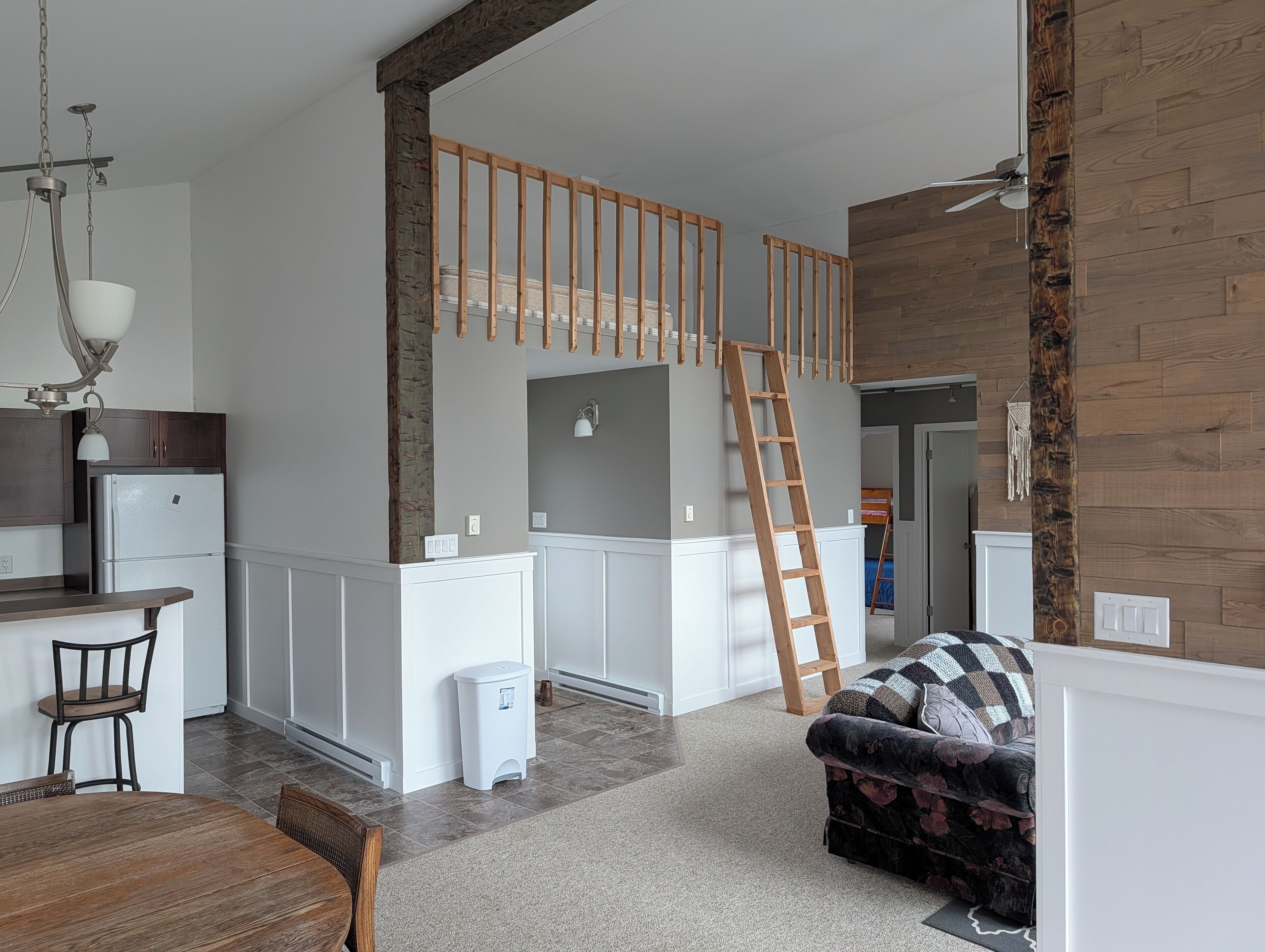 A modern kitchen with white cabinets, a wooden ladder, and a dining area with a table and chairs.