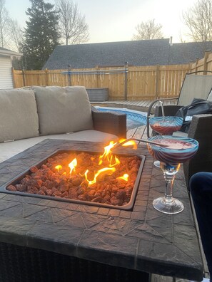 A patio with a fire feature, outdoor seating, and a pool in the background. - Eva Blue Manor (New Maryland)