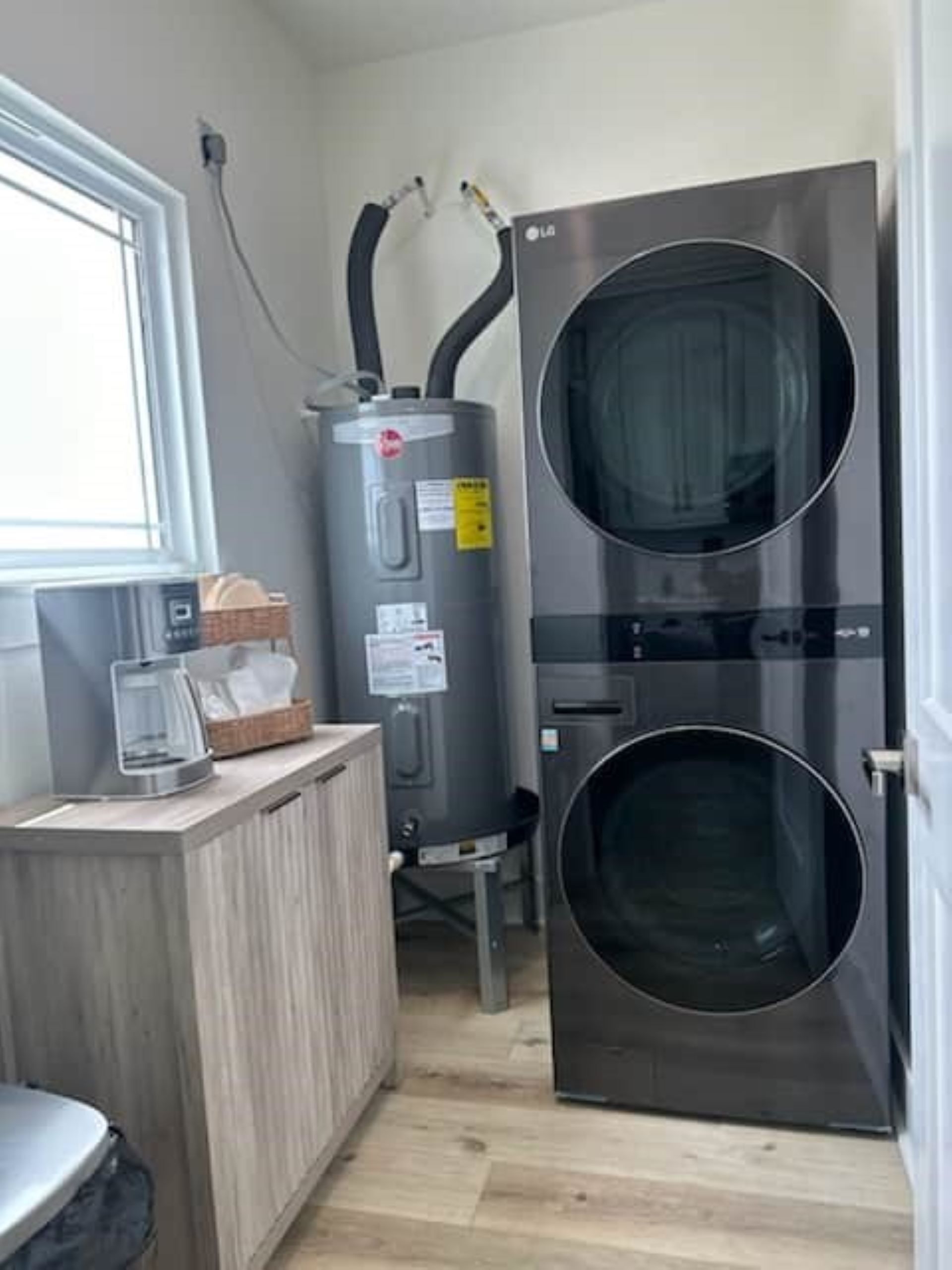 A compact laundry room with a large, modern washer and dryer, a small countertop with a coffee maker, and a window providing natural light.