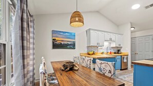 Un coin repas avec une table en bois, des chaises à motifs, un luminaire suspendu et une cuisine en arrière-plan.