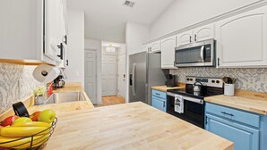 Une cuisine moderne avec des meubles blancs, un réfrigérateur en acier inoxydable, un four à micro-ondes et un plan de travail en bois.