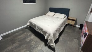 Une chambre à coucher avec un lit, une table de chevet, une petite armoire en bois et un tableau accroché au mur.