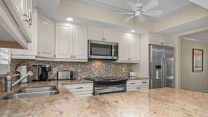 Una cocina moderna con armarios blancos, encimera de granito, refrigerador de acero inoxidable y un microondas.