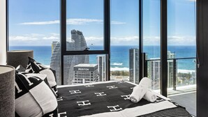 Ein Schlafzimmer mit großem Fenster, einem Bett mit schwarz-weiß gestreiftem Überwurf und Blick auf das Meer und hohe Gebäude.