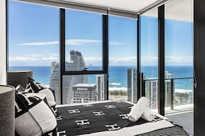 Ein Schlafzimmer mit großem Fenster, einem Bett mit schwarz-weiß gestreiftem Überwurf und Blick auf das Meer und hohe Gebäude.