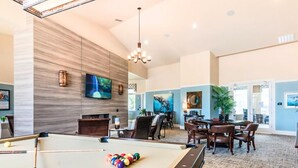Une table de billard avec des billes, un téléviseur et un coin repas avec des chaises et des tables.