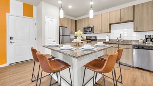 Une cuisine moderne dotée d’un îlot central, d’appareils électroménagers en acier inoxydable et d’armoires en bois.