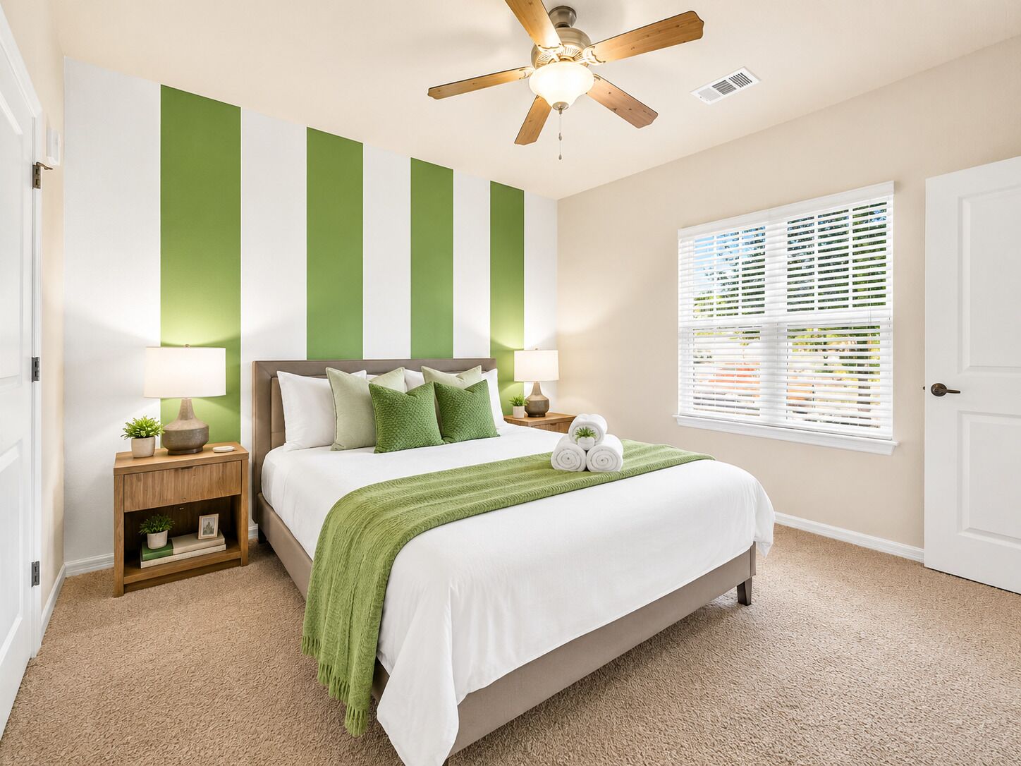 A bedroom with a bed, nightstands, a ceiling fan, a window with blinds, and a green wall accent.
