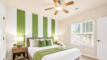 A bedroom with a bed, nightstands, a ceiling fan, a window with blinds, and a green wall accent.