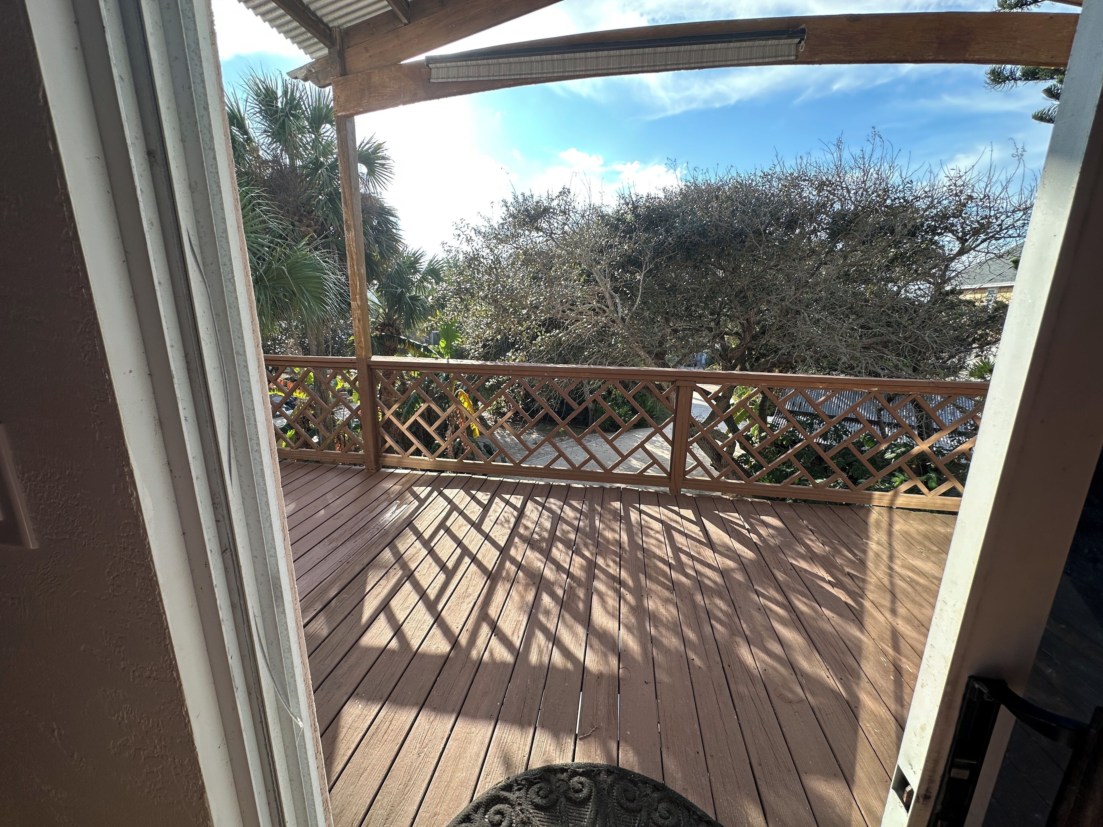 A wooden deck with a lattice railing, surrounded by trees and shrubs.