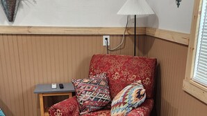 A cozy living room with a red patterned sofa, a colorful geometric rug, a small wooden side table, and a wicker storage box. - Cozy 1-bedroom studio  in Texico, Nm. (Texico)