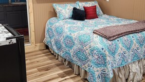 A bedroom with a bed, a television mounted on the wall, a wooden cabinet, and a patterned rug. - Cozy 1-bedroom studio  in Texico, Nm. (Texico)