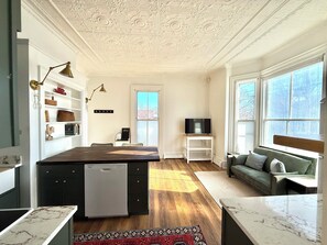 A modern kitchen with a marble countertop, a built-in dishwasher, and a white refrigerator. - Hip Historical First Fl 1BR Downtown King size bed (Brunswick)