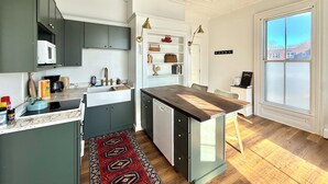 A modern kitchen with a built-in microwave, a coffee maker, and a sink. There is a dining area with a wooden table and chairs. - Hip Historical First Fl 1BR Downtown King size bed (Brunswick)