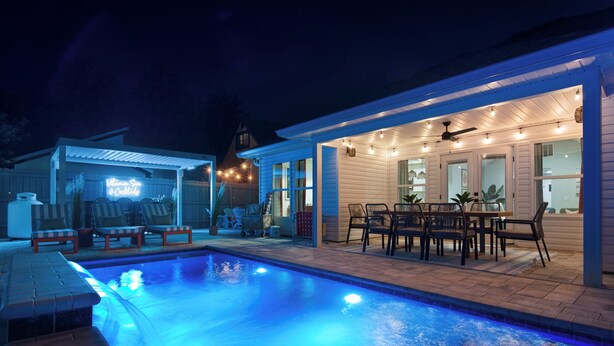 En swimmingpool med terrasse, udendørs møbler og et overdækket spiseområde.