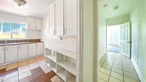 Eine Küche mit weißen Schränken, Fliesenboden und einem Fenster mit Jalousien.