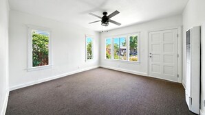 Ein geräumiges Zimmer mit weißen Wänden, einem Deckenventilator und großen Fenstern mit Blick ins Grüne.