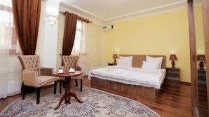 Quarto de hotel com cama, duas poltronas, uma mesinha redonda com bule e tapete estampado.