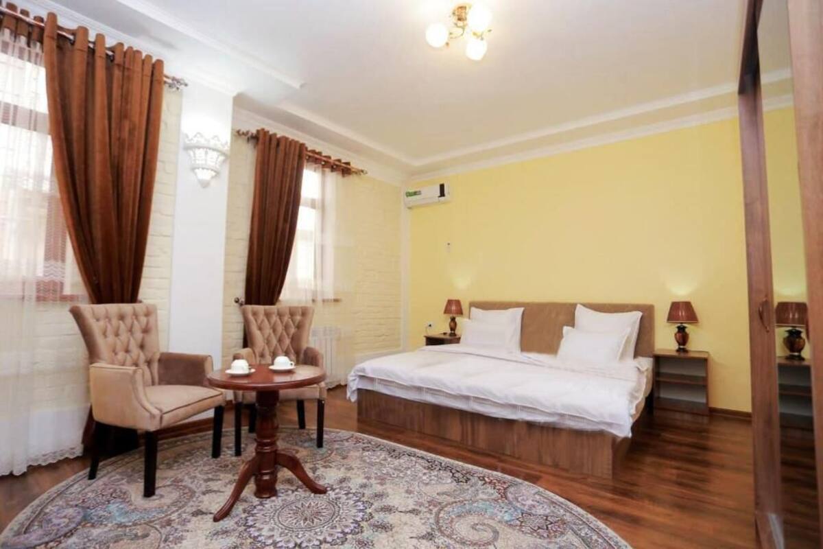 Ett hotellrum med en säng, två fåtöljer, ett litet runt bord med en tekanna och en mönstrad matta.