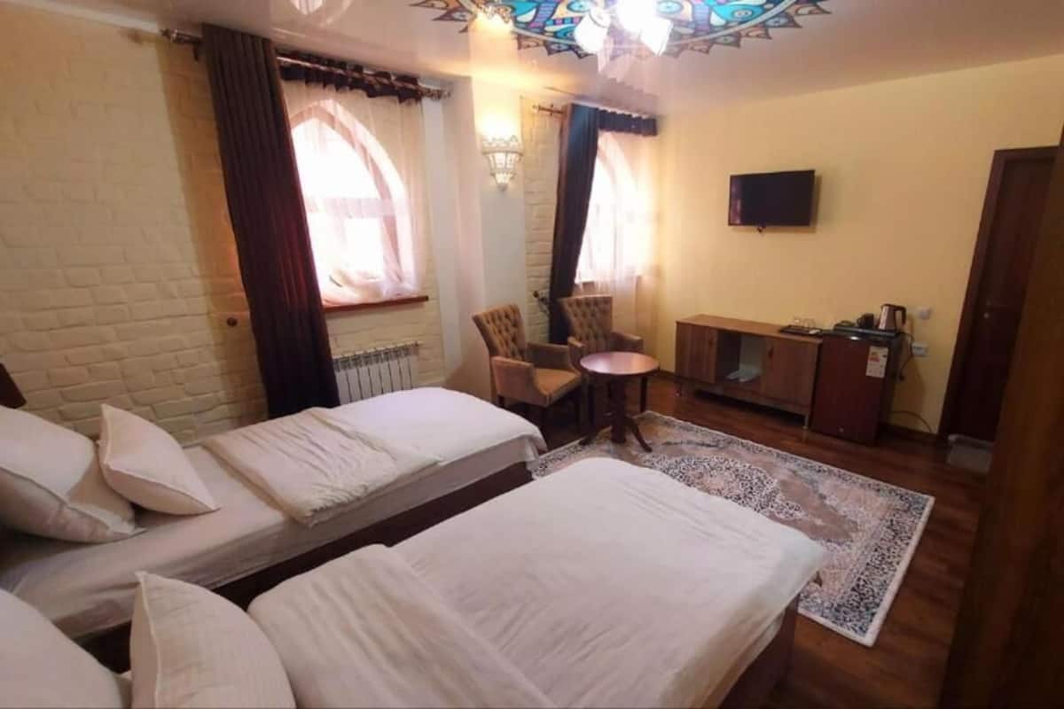 Ett hotellrum med två separata sängar, ett litet bord, en stol, en TV och ett fönster med gardiner.