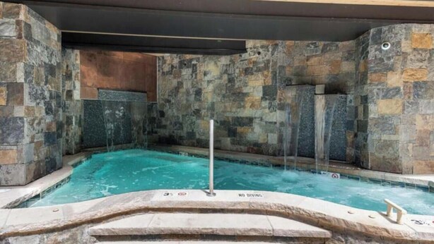 A hot tub with a stone wall backdrop, a no diving sign, and a metal pole. - Park Plaza Condo W/Resort Amenities (Beaver Creek)