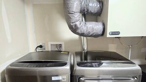 Dos electrodomésticos de acero inoxidable, probablemente una lavadora y secadora, en una habitación pequeña con una pared blanca y un enchufe visible.