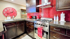 Una cocina moderna con armarios de madera oscura, salpicadero de baldosas rojas, un reloj grande rojo y una estufa a gas.