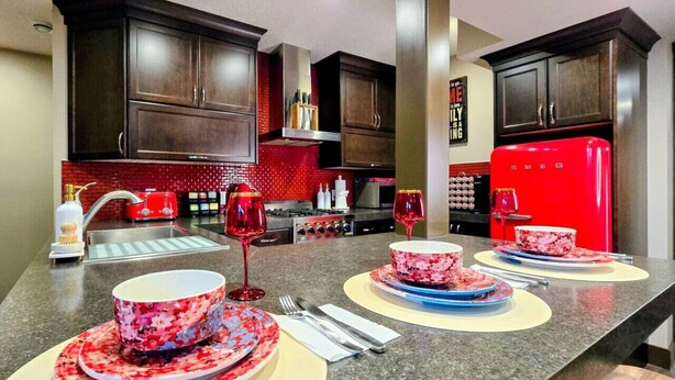 Una cocina moderna con armarios de madera oscura, un refrigerador rojo y una encimera de granito.