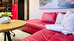 Un sofá rojo con una manta blanca y un jarrón de flores blancas sobre una mesa de madera.