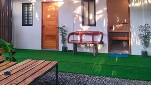 Una casa de dos pisos con un balcón, una puerta de madera, un banco y una pequeña mesa.