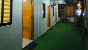 Un pasillo con puertas que dan a habitaciones, alfombra verde y luces en el techo.