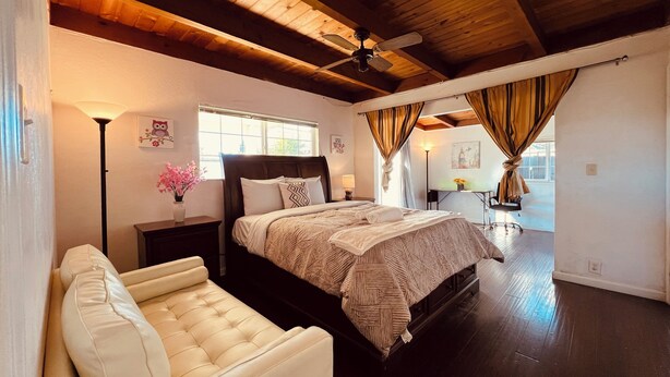 Ein Schlafzimmer mit einem großen Bett, einem Schreibtisch, einem Sessel, einer Stehlampe und einem Deckenventilator.