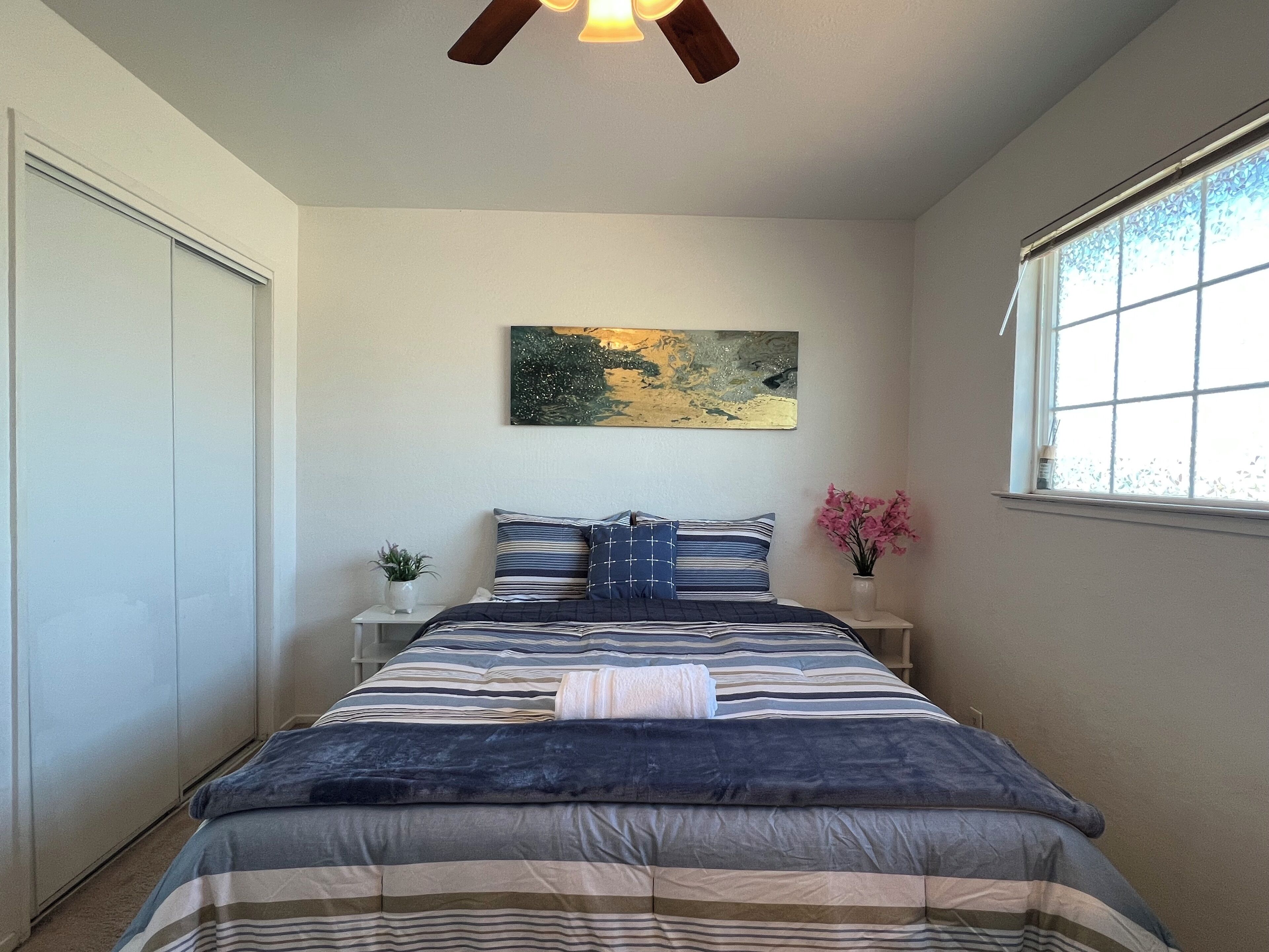 A bedroom with a bed, a nightstand, a window, and a ceiling fan.