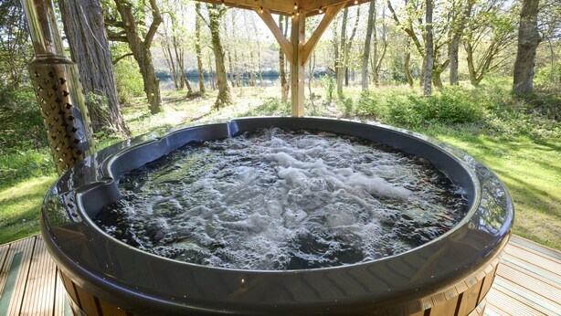 A hot tub outdoors with a wooden deck and trees in the background. - Lochside hideaway with hot tub by Loch Ness (Inverness)