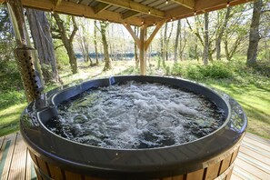 A hot tub outdoors with a wooden deck and trees in the background. - Lochside hideaway with hot tub by Loch Ness (Inverness)