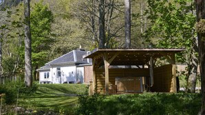 A cabin with a wooden deck, a hot tub, and a covered area with string lights. - Lochside hideaway with hot tub by Loch Ness (Inverness)