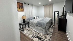 Une chambre à coucher moderne avec un lit, une table de chevet, une lampe et un miroir.