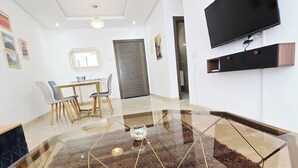 Una sala de estar moderna con una mesa de centro de vidrio, un televisor de pantalla plana montado en la pared y un comedor con sillas y una mesa.