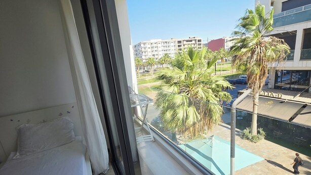 Un balcón con una cama, vistas a palmeras y una piscina.
