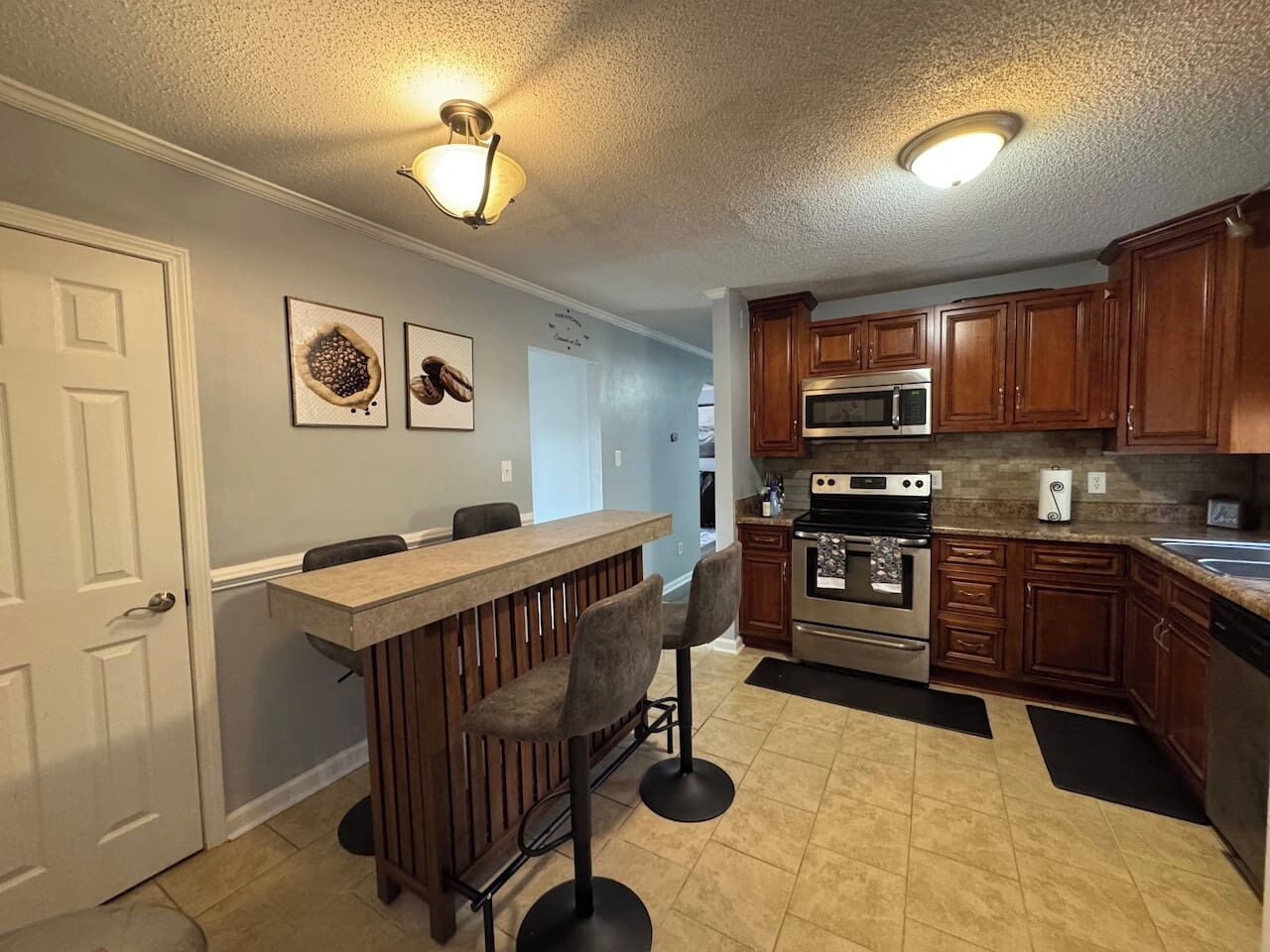 A kitchen with wooden cabinets, a stainless steel oven, a microwave, and a bar area with stools.