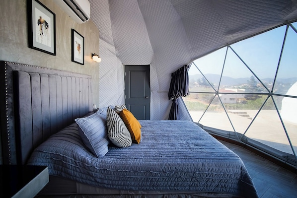 Un dormitorio con una cama grande, un cabecero, una puerta y una ventana con vistas al paisaje.