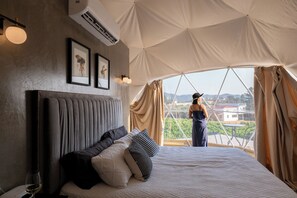 Habitación tipo alojamiento en tienda de campaña, con cama, almohadas, un cuadro enmarcado, equipo de aire acondicionado y vistas al paisaje.