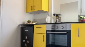 Een keuken met gele kastjes, een zwarte koelkast en een roestvrijstalen oven.