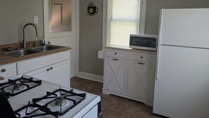 A kitchen with white cabinets, a gas stove, a microwave, and a refrigerator. - Cozy 2-bedroom cottage in charming Council Bluffs with AC (Council Bluffs)