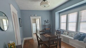 A dining area with a wooden table and chairs, a ceiling light fixture, and a window with blinds. - Cozy 2-bedroom cottage in charming Council Bluffs with AC (Council Bluffs)