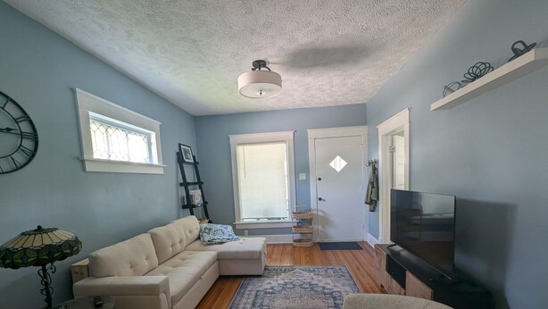 A living room with a beige sectional sofa, a small round table, a patterned rug, a television, and a ceiling fan. - Cozy 2-bedroom cottage in charming Council Bluffs with AC (Council Bluffs)